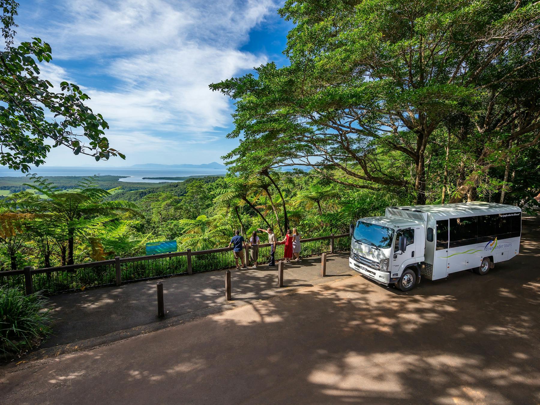 Passengers standing at Alexandra Lookout with view of rainforest canopy out to the ocean in distance