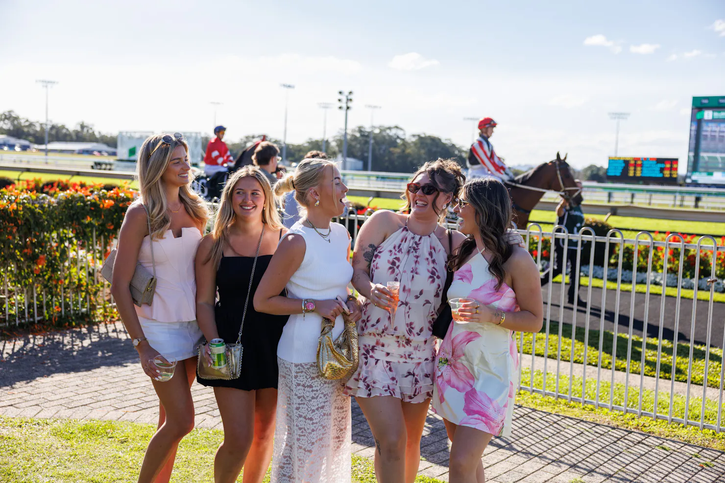 Group of girls all looking at each other smiling and laughing on the grass with a horse in the back