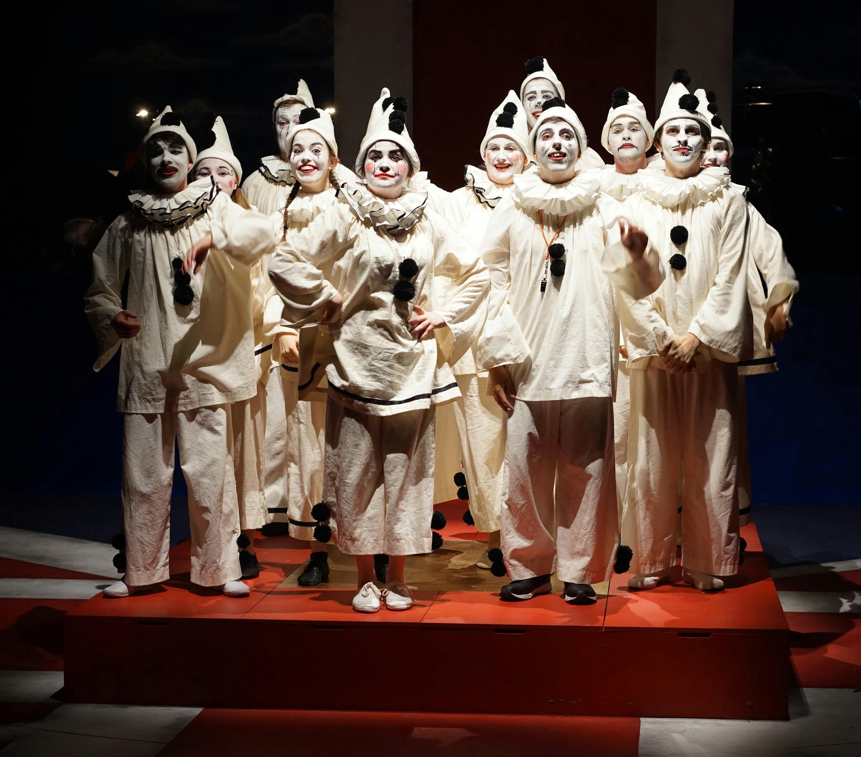 group of 12 young people dressed as clowns in all white with black pompoms and white make-up