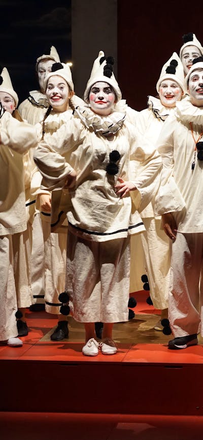 group of 12 young people dressed as clowns in all white with black pompoms and white make-up