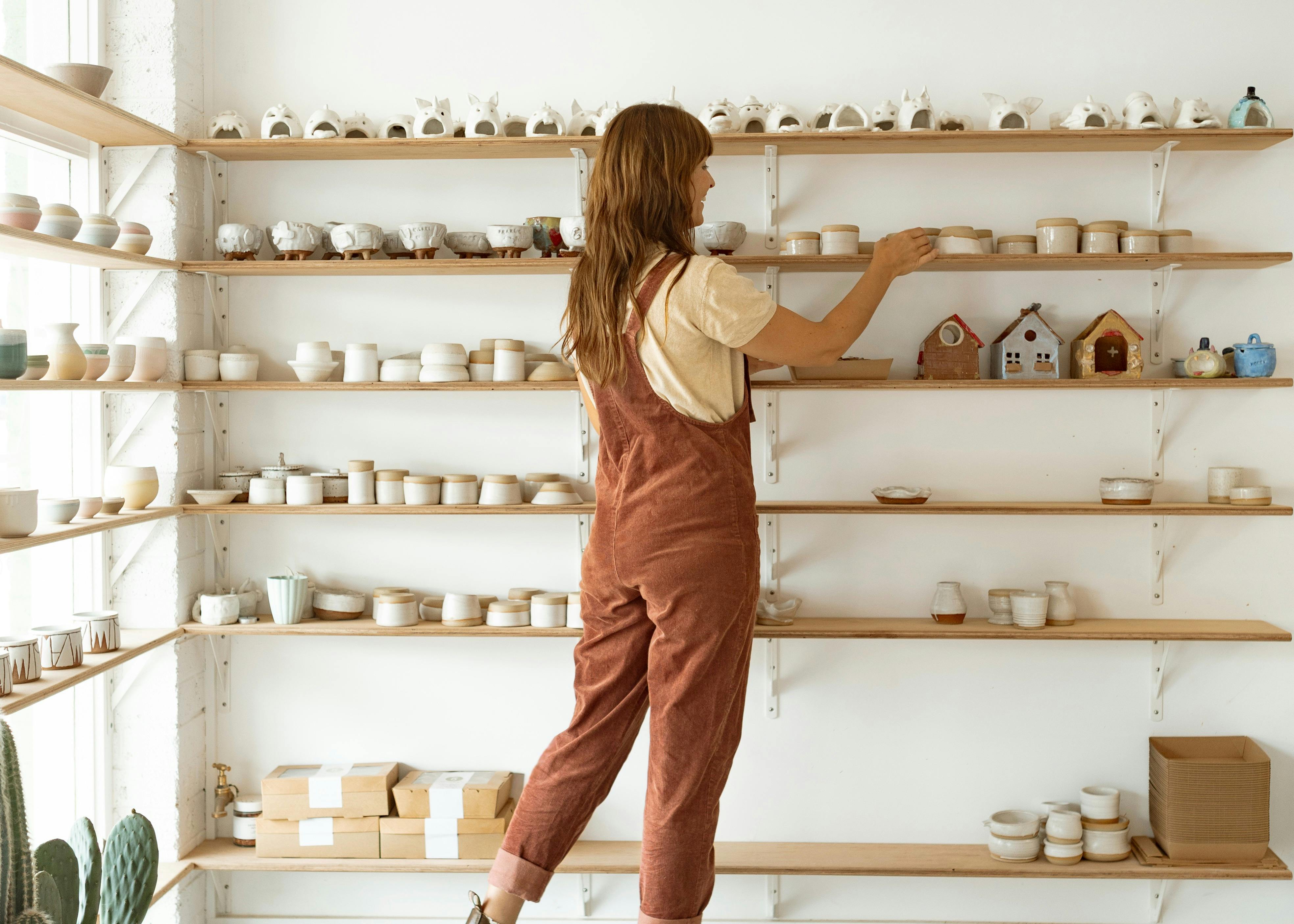 Woman arranges pottery items on a shelf at Silt Studio
