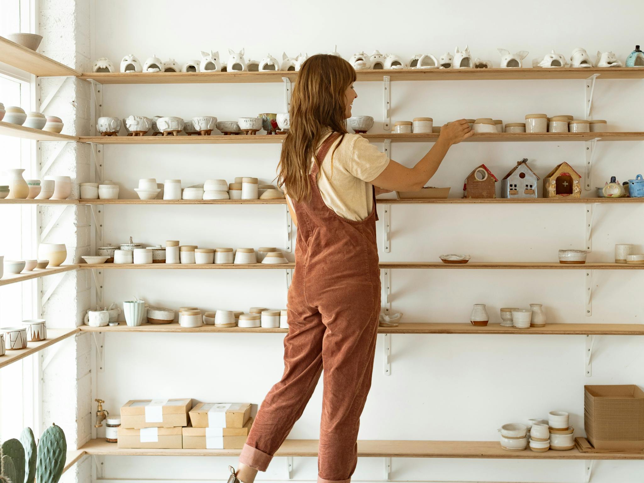 Woman arranges pottery items on a shelf at Silt Studio