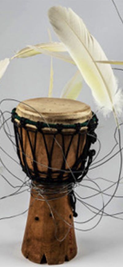 Brown African drum with white feathers which have been attached with wire
