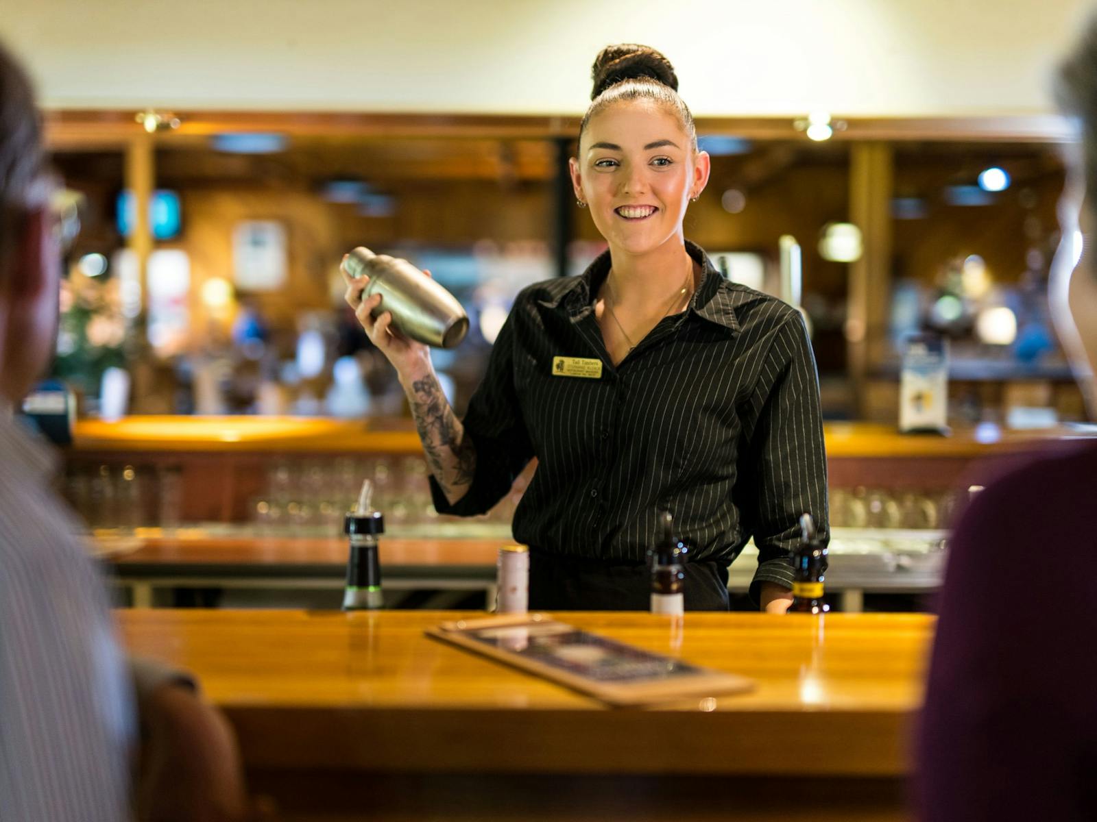 Young woman smiling at guests as she mixes a cocktail in a shaker at the bar between lounge & bistro