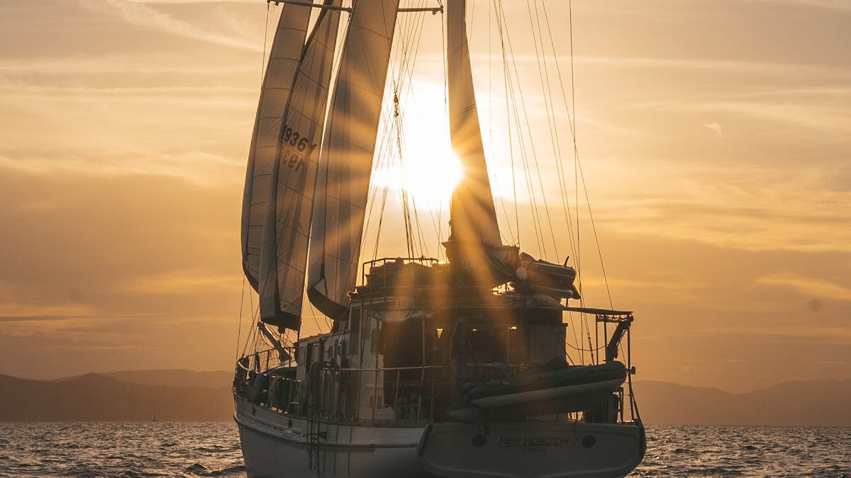 Sailing yacht silhouetted against a golden sunset on the calm waters of the Whitsundays
