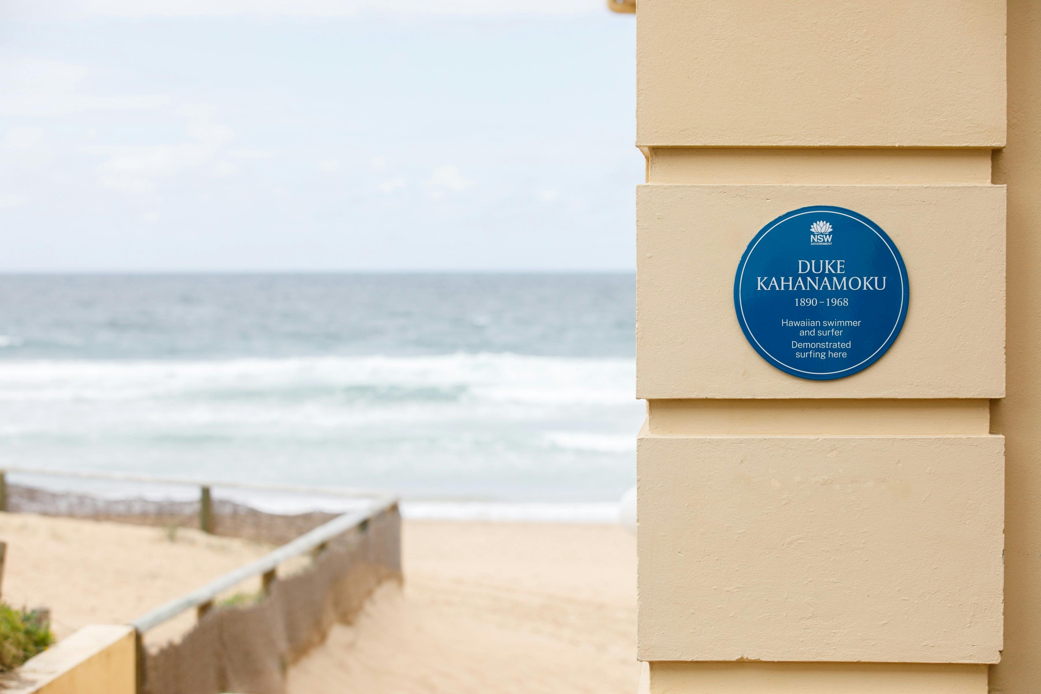 Blue plaque on cream coloured exterior wall with beach in the back ground