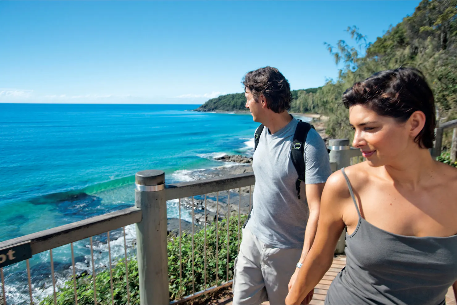 Couple walking along boardwalk on coast.