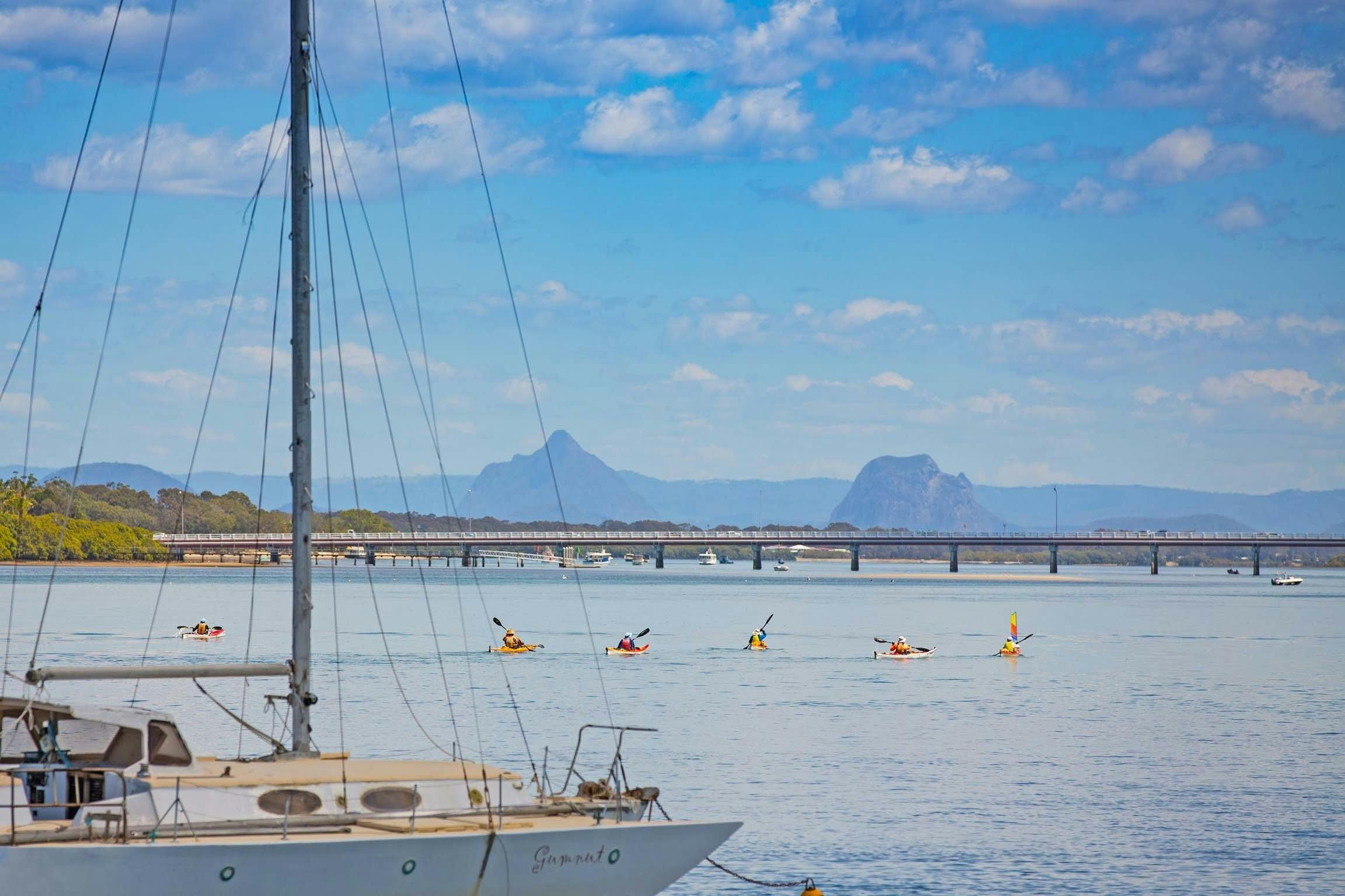 A number of people Kayaking with views of the Bribie Island Bridge and Glasshouse Mountains