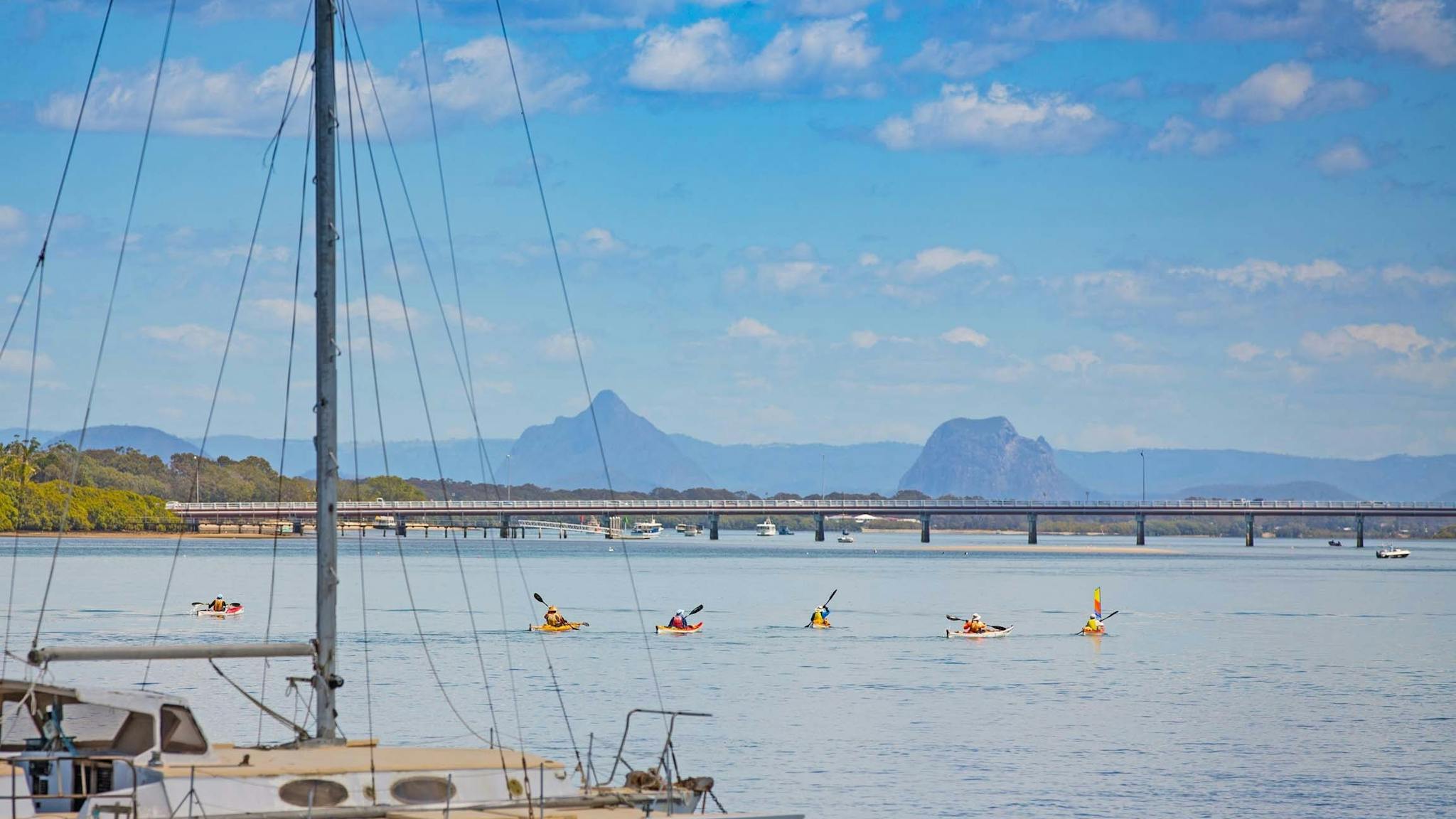 A number of people Kayaking with views of the Bribie Island Bridge and Glasshouse Mountains