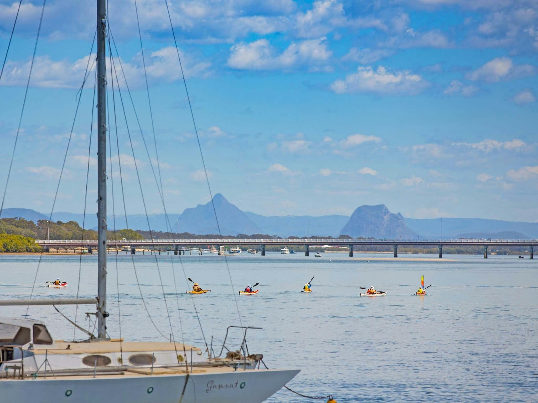 A number of people Kayaking with views of the Bribie Island Bridge and Glasshouse Mountains