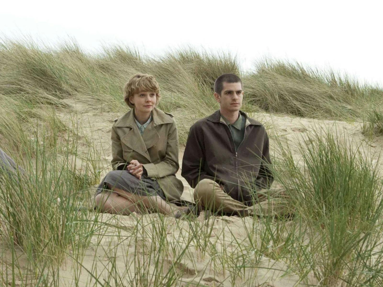 One woman and one man sitting rugged up in coats on a beach