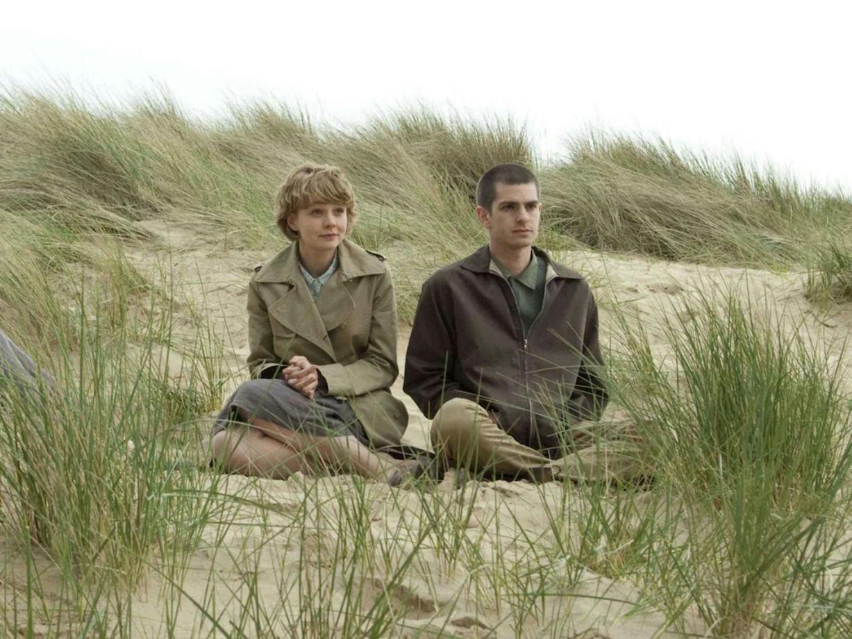 One woman and one man sitting rugged up in coats on a beach