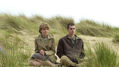 One woman and one man sitting rugged up in coats on a beach