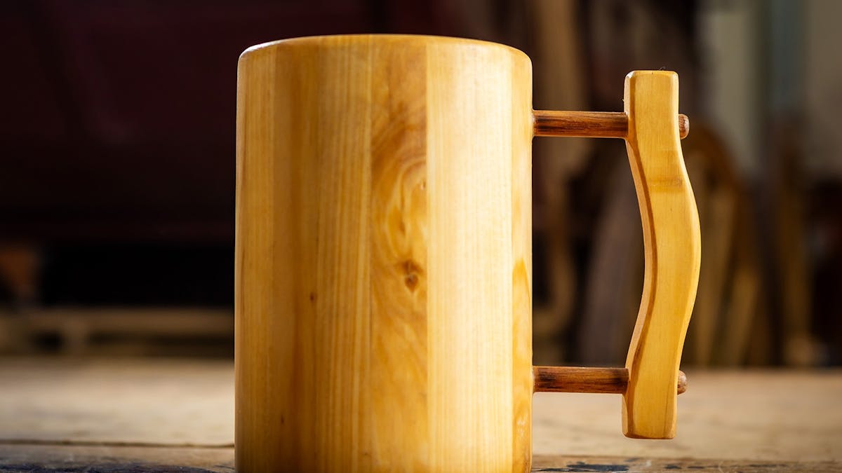 Handcrafted wooden tankard with handle displayed on table.