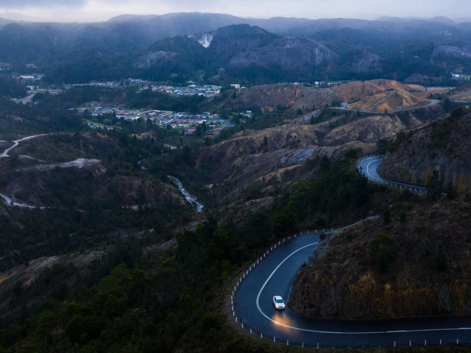 A vehicle drives away from Queenstown at night along a winding road