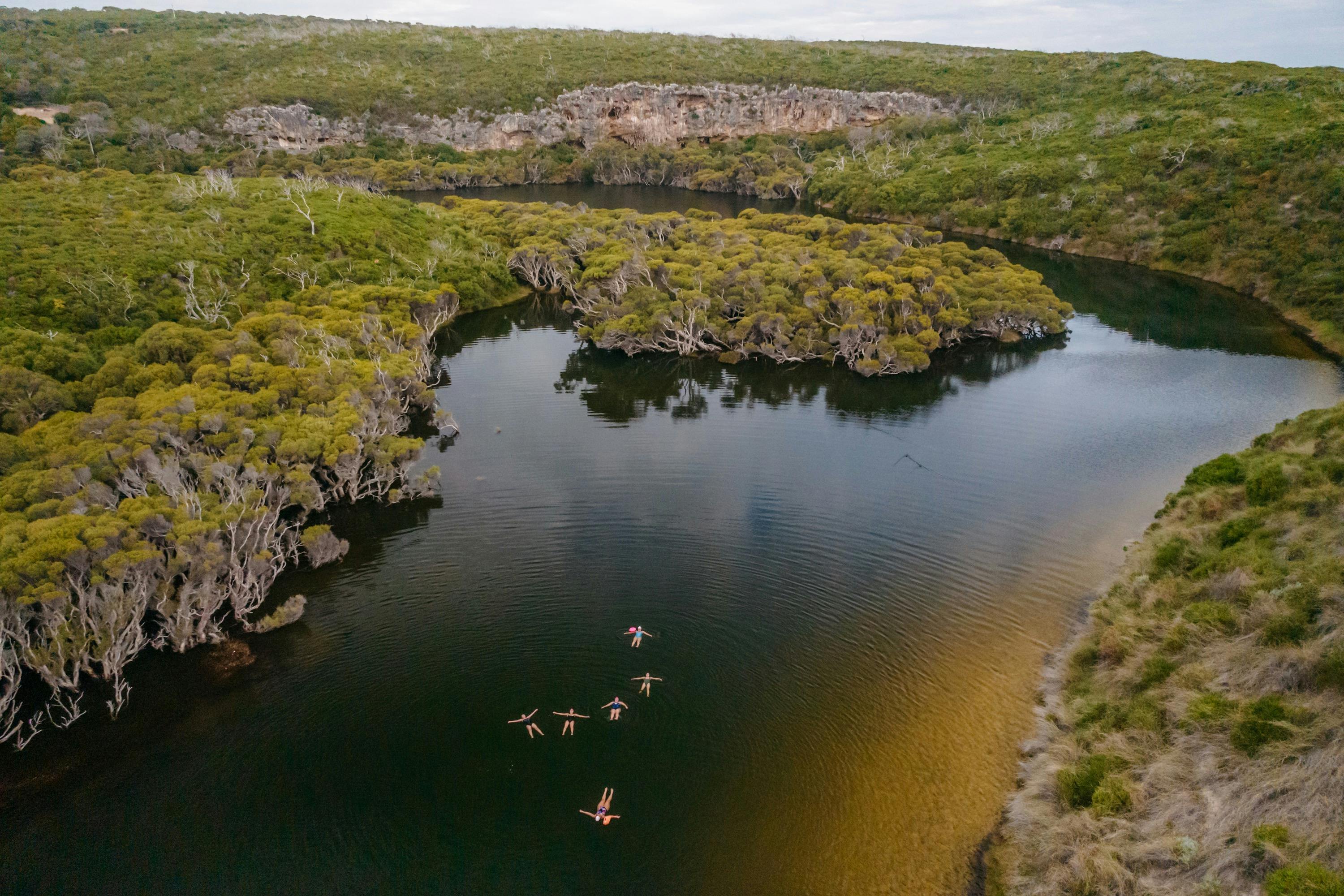 swimmers swim in the calm waters of a river banked by cliffs and trees