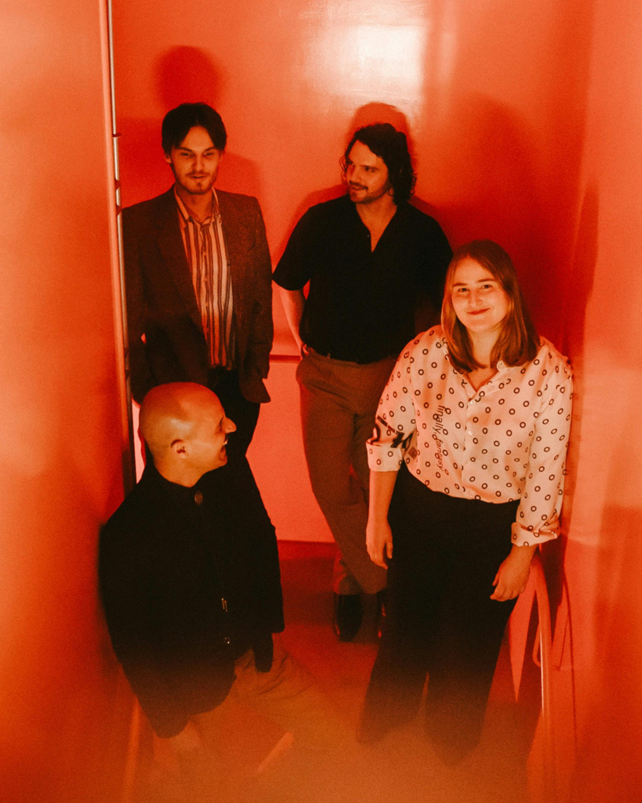 The quartet standing in a small red lit room, wearing formal attire.