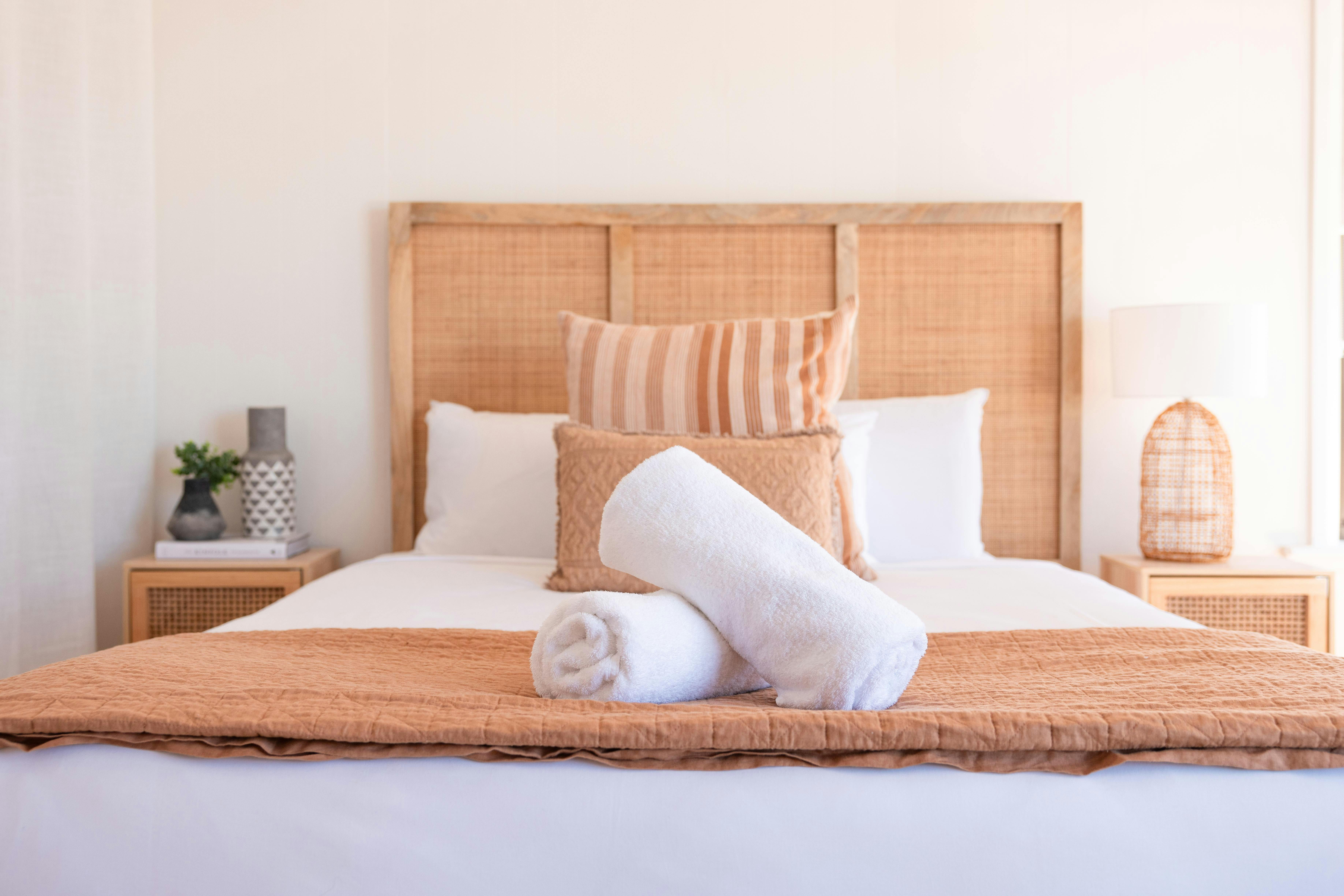 Inviting bed with a woven headboard, layered pillows, rolled towels, and warm-toned bedding