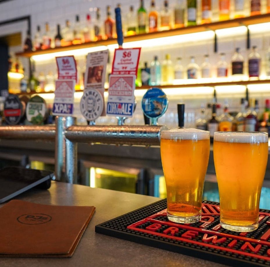Two beers sitting on a bar in front of the bar taps