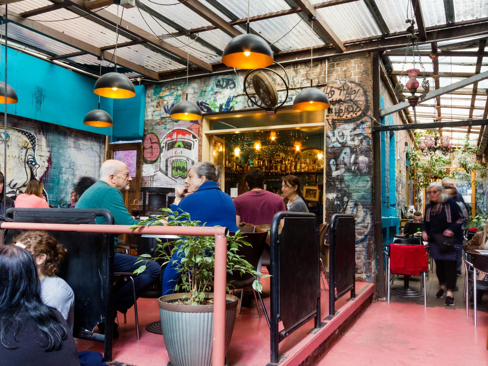 A bar set into a wall of graffiti, looking out onto covered deck with customers.