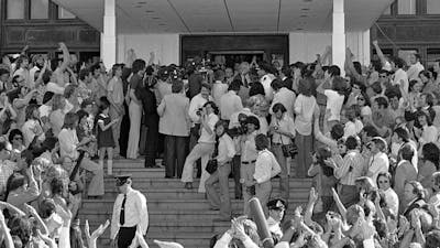 A large crowd of people and press stand below and on the steps of Old Parliament House.