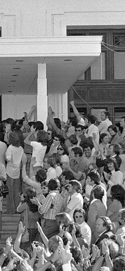 A large crowd of people and press stand below and on the steps of Old Parliament House.