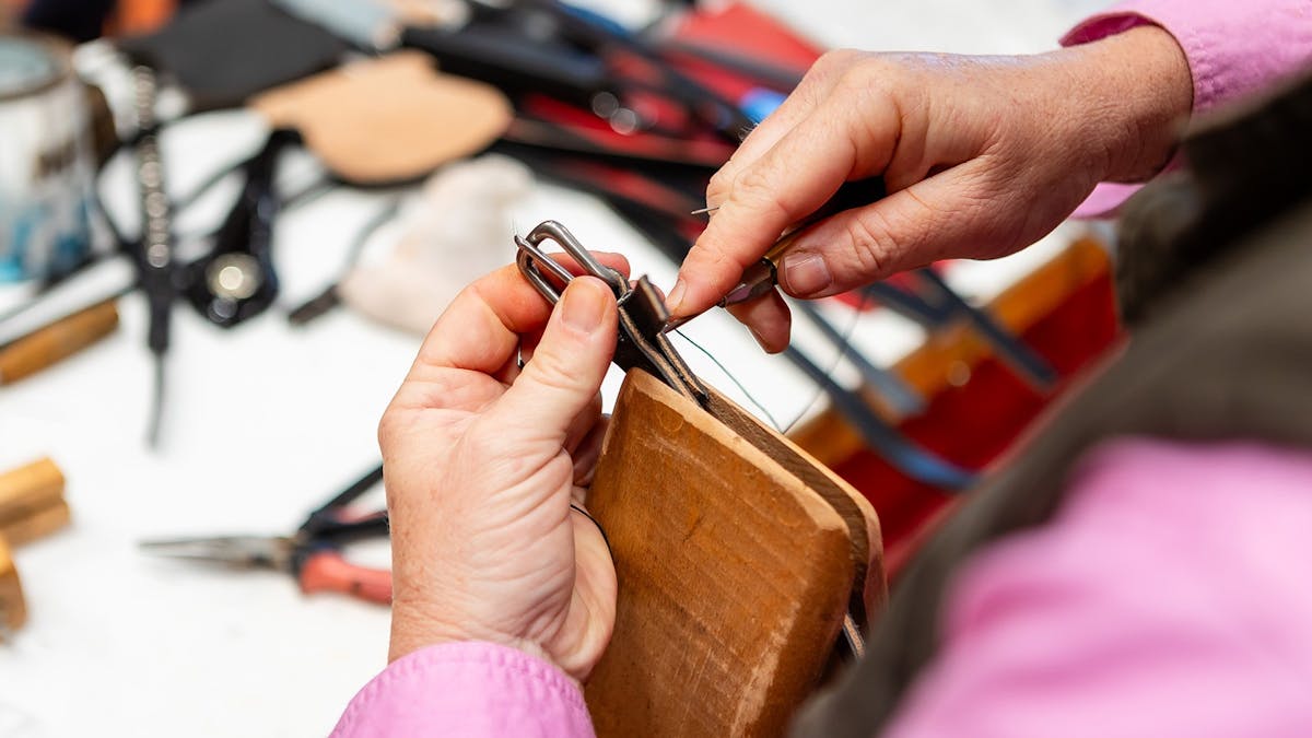Woman using tools to sew leather bridle piece.