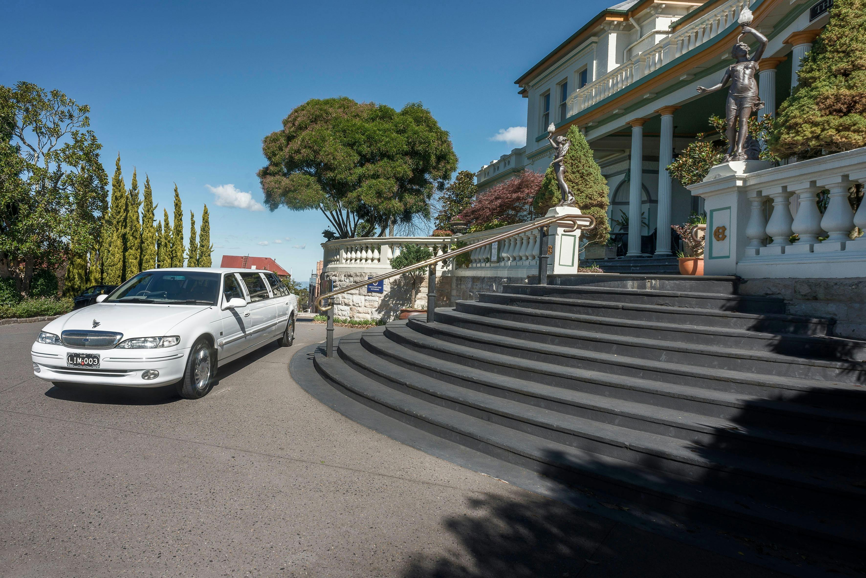White stretch limousine at the base of steps with historic hotel in the background