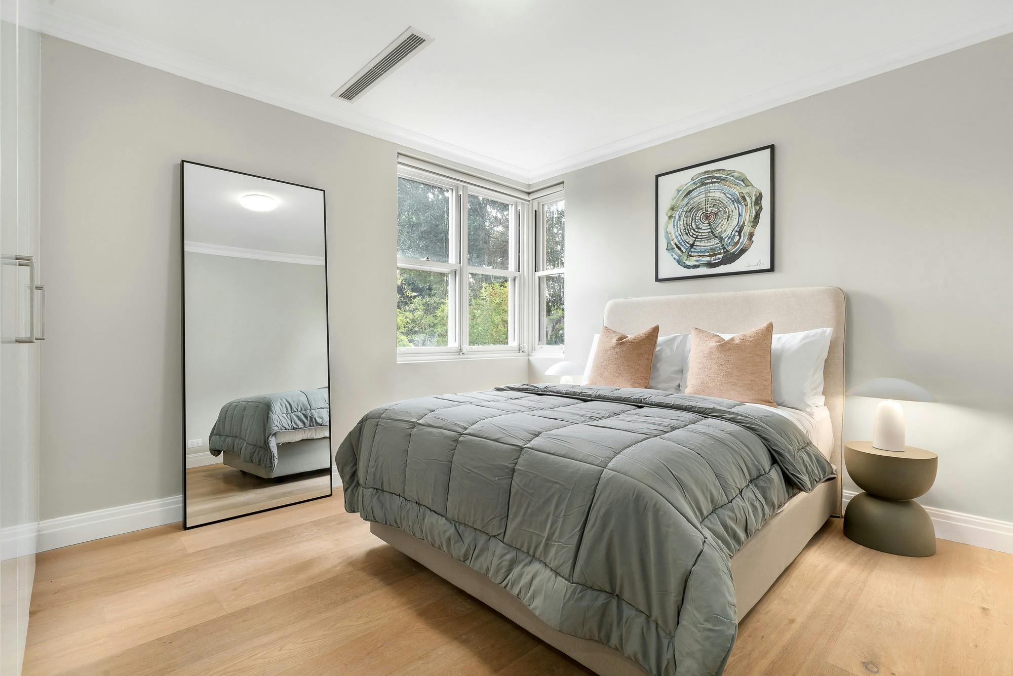 Modern, spacious bedroom with large window and full length mirror, queen sized bed and side tables.