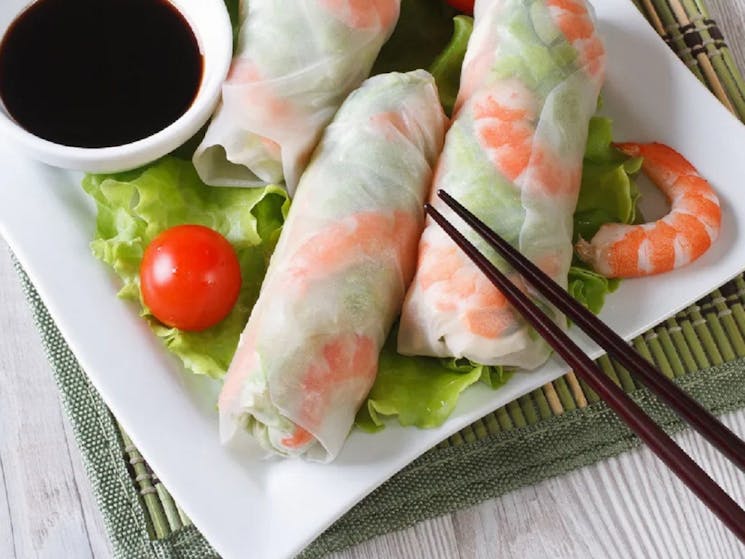 Image of 3 prawn rice paper rolls with hoisin sauce and chopsticks
