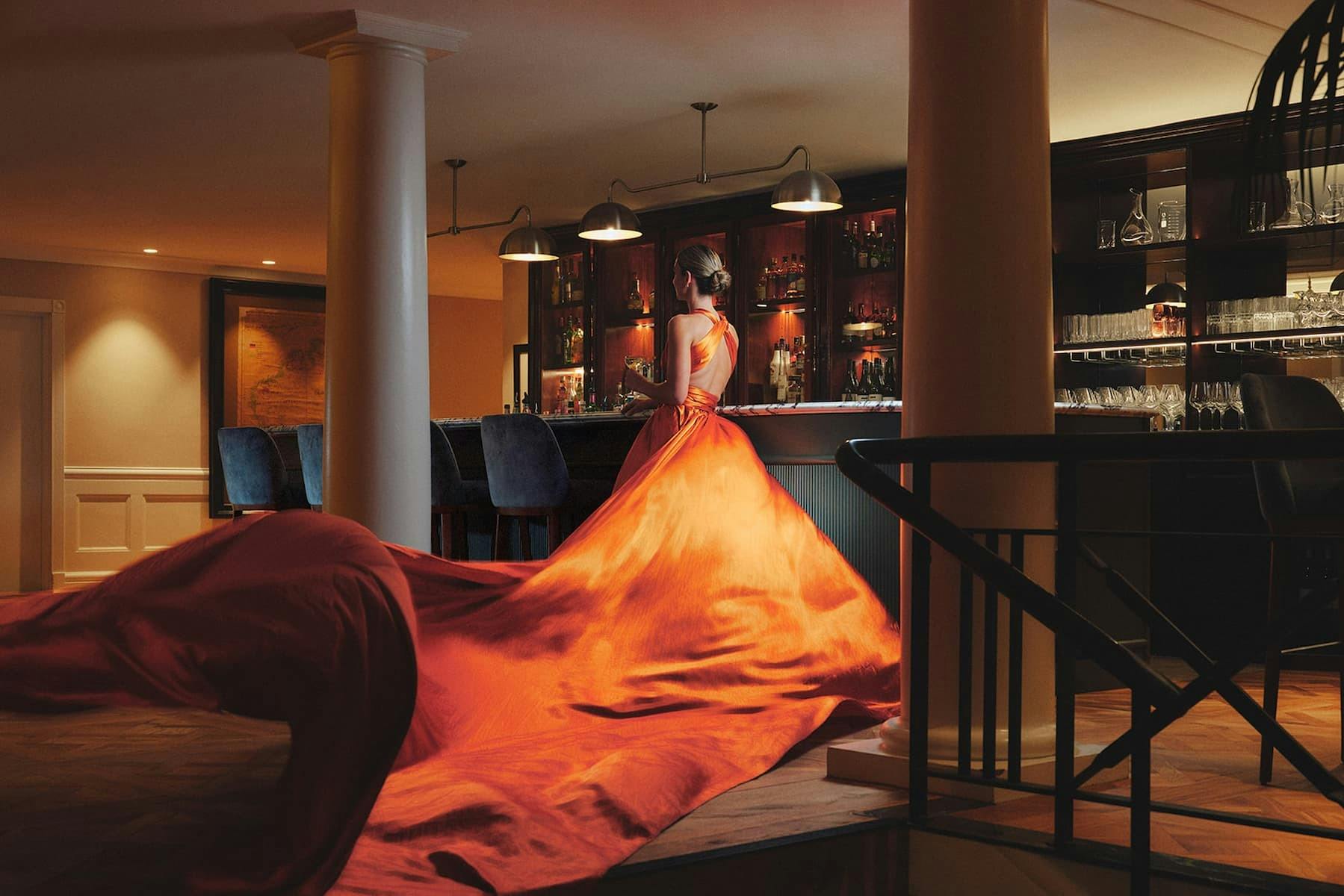 Woman in long orange dress next to the mahogany bar at Ardour Lilianfels