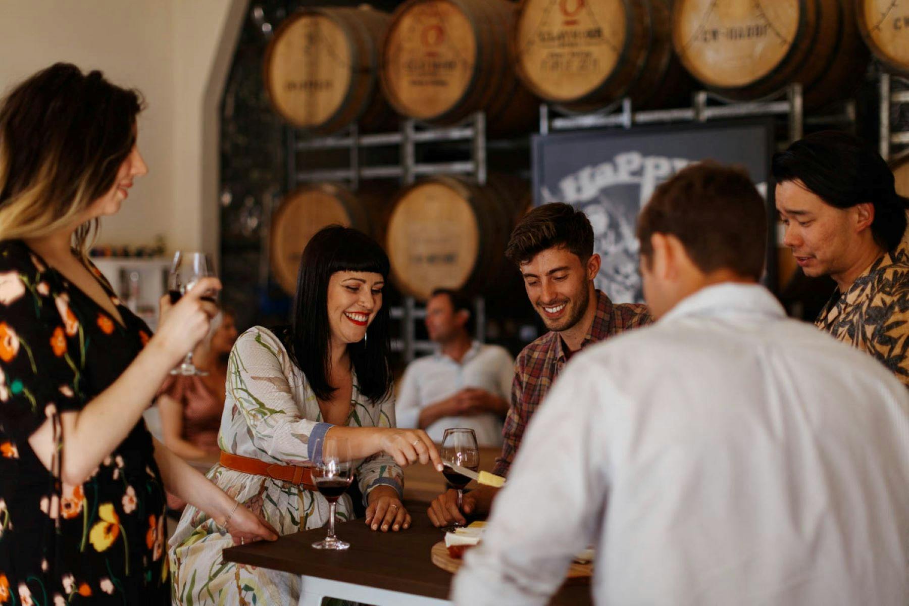 a group of people seated and standing drinking wine and sharing a platter