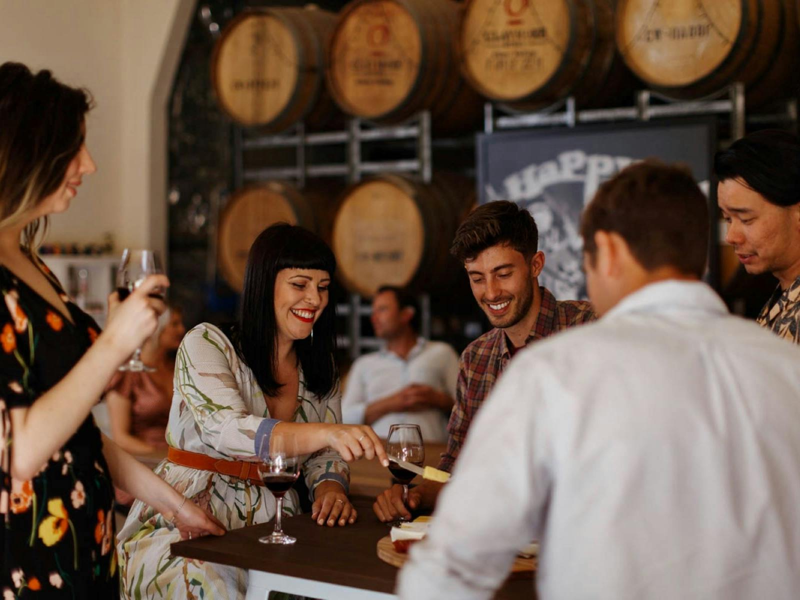 a group of people seated and standing drinking wine and sharing a platter