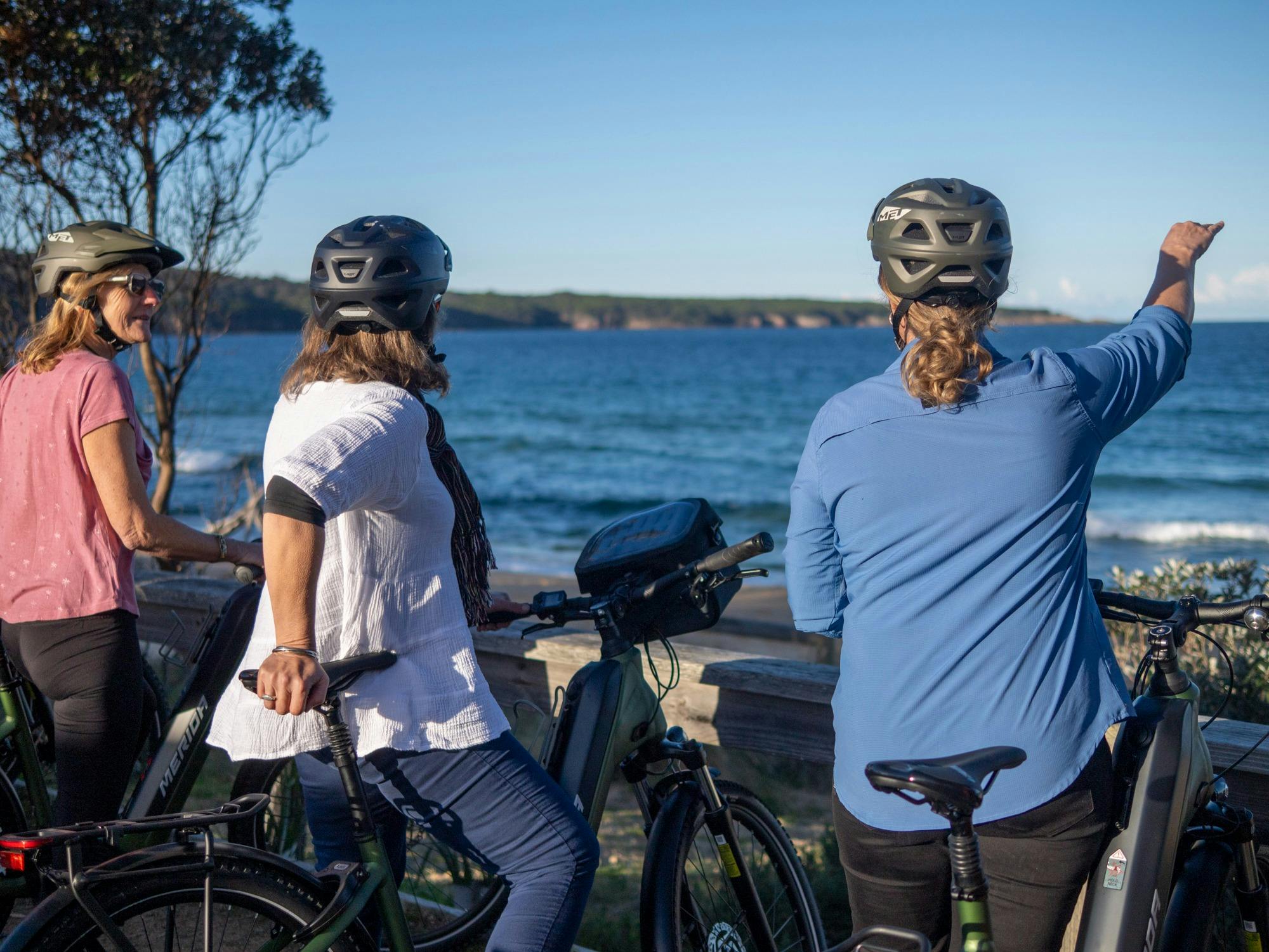 Guide with two guests on e-bikes with Aslings Beach in background