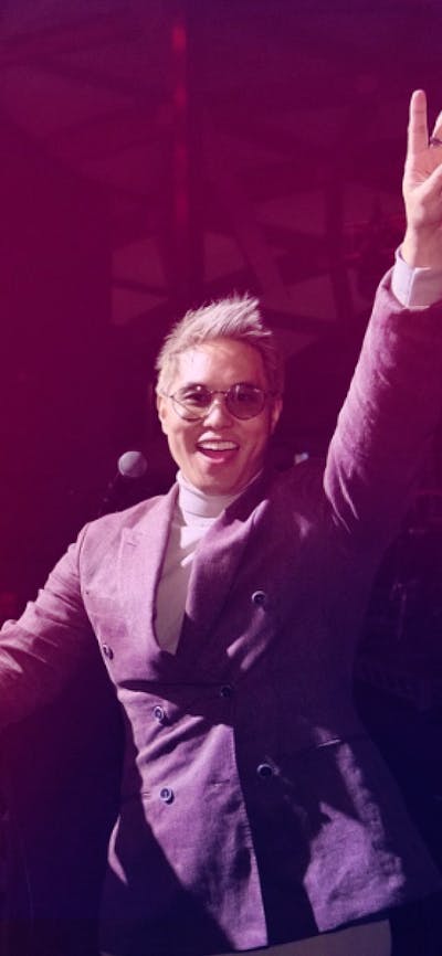 Andy Trieu doing a live DJ set  on stage doing a peace sign