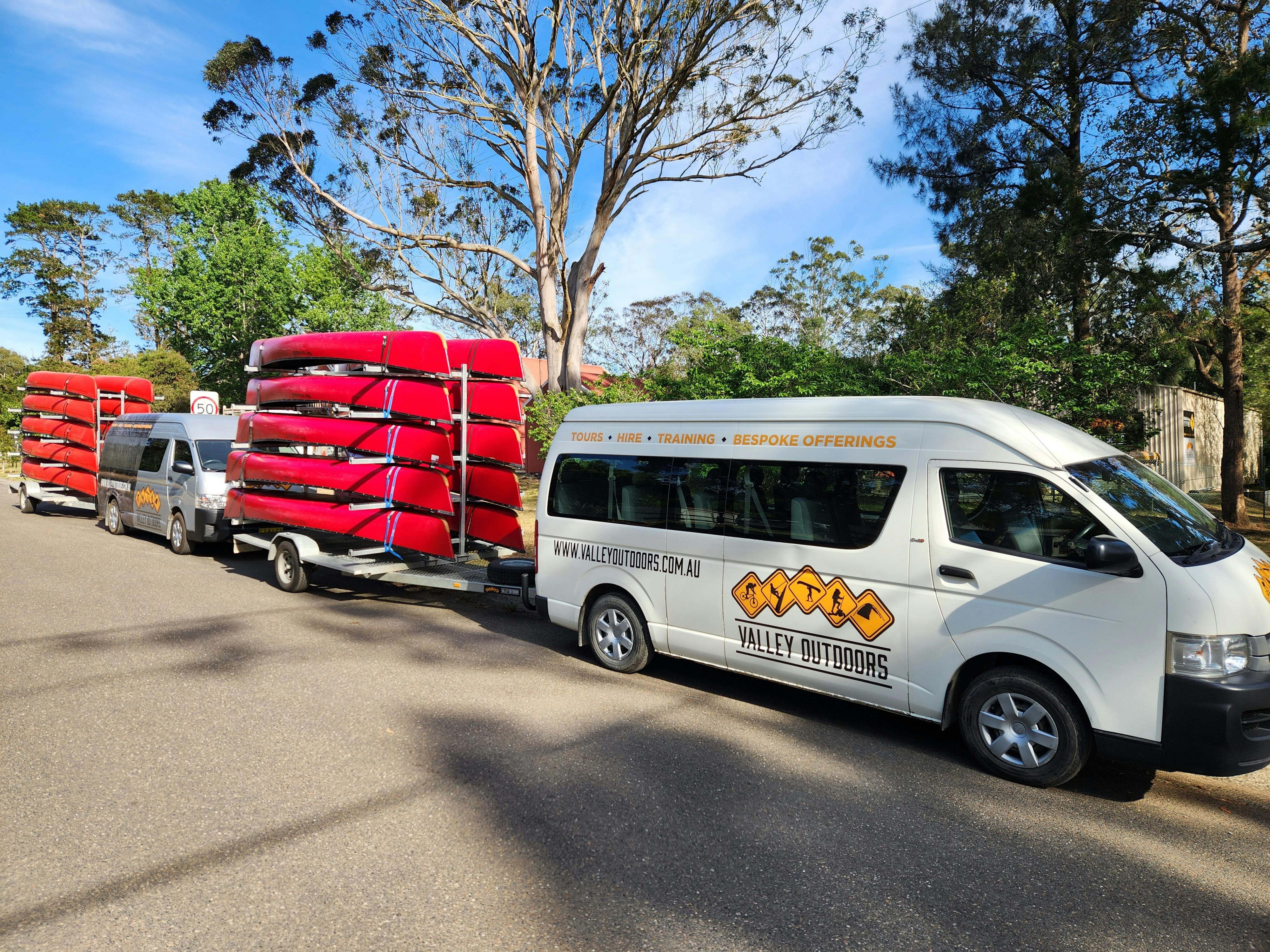 White van with Valley Outdoors logo towing a trailer with 10 red canoes on it