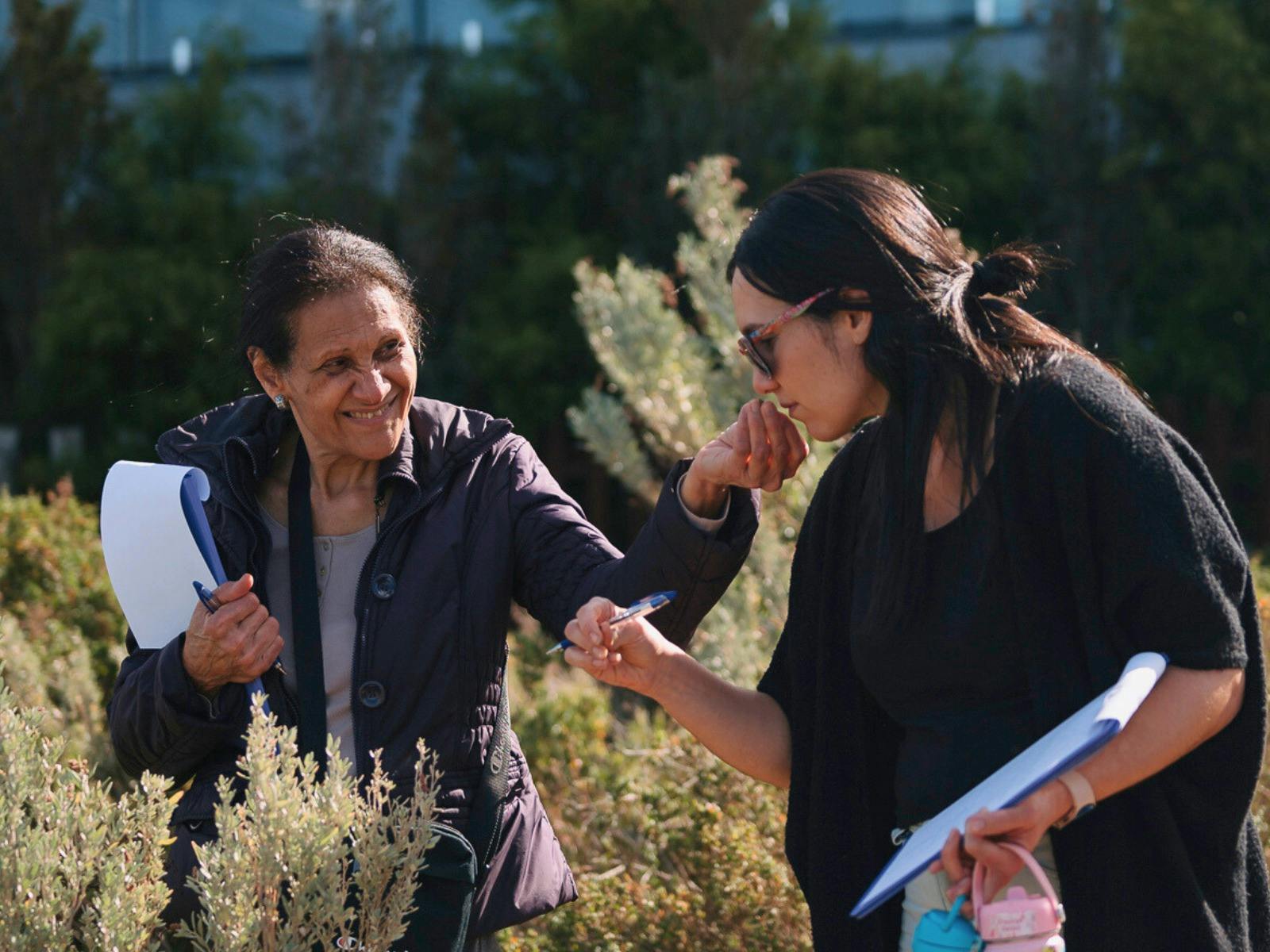 two woman smelling a plant and taking notes