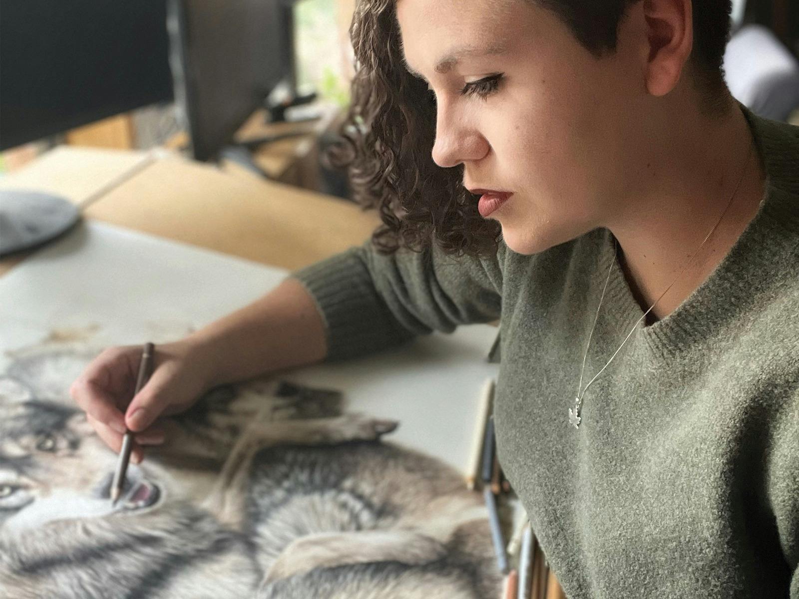 Artist in green, drawing a pack of wolves on the table behind her.