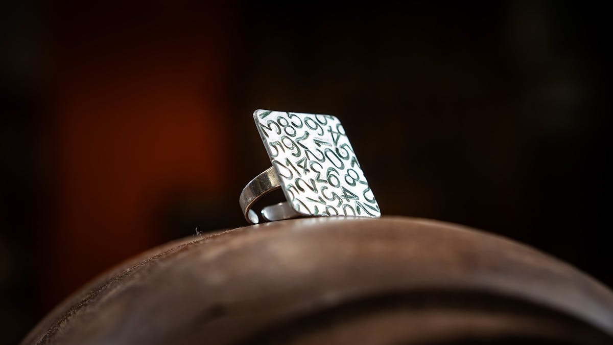 Close-up of handcrafted metal ring with square face and numbers etched on to make pattern.