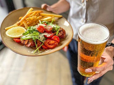 Hands holding a plate of chicken with fries and salad, and a glass of beer.