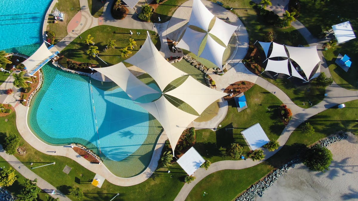 Aerial photo of Airlie Beach Lagoon showing swimming pool with bridge path,  gardens and shade saili
