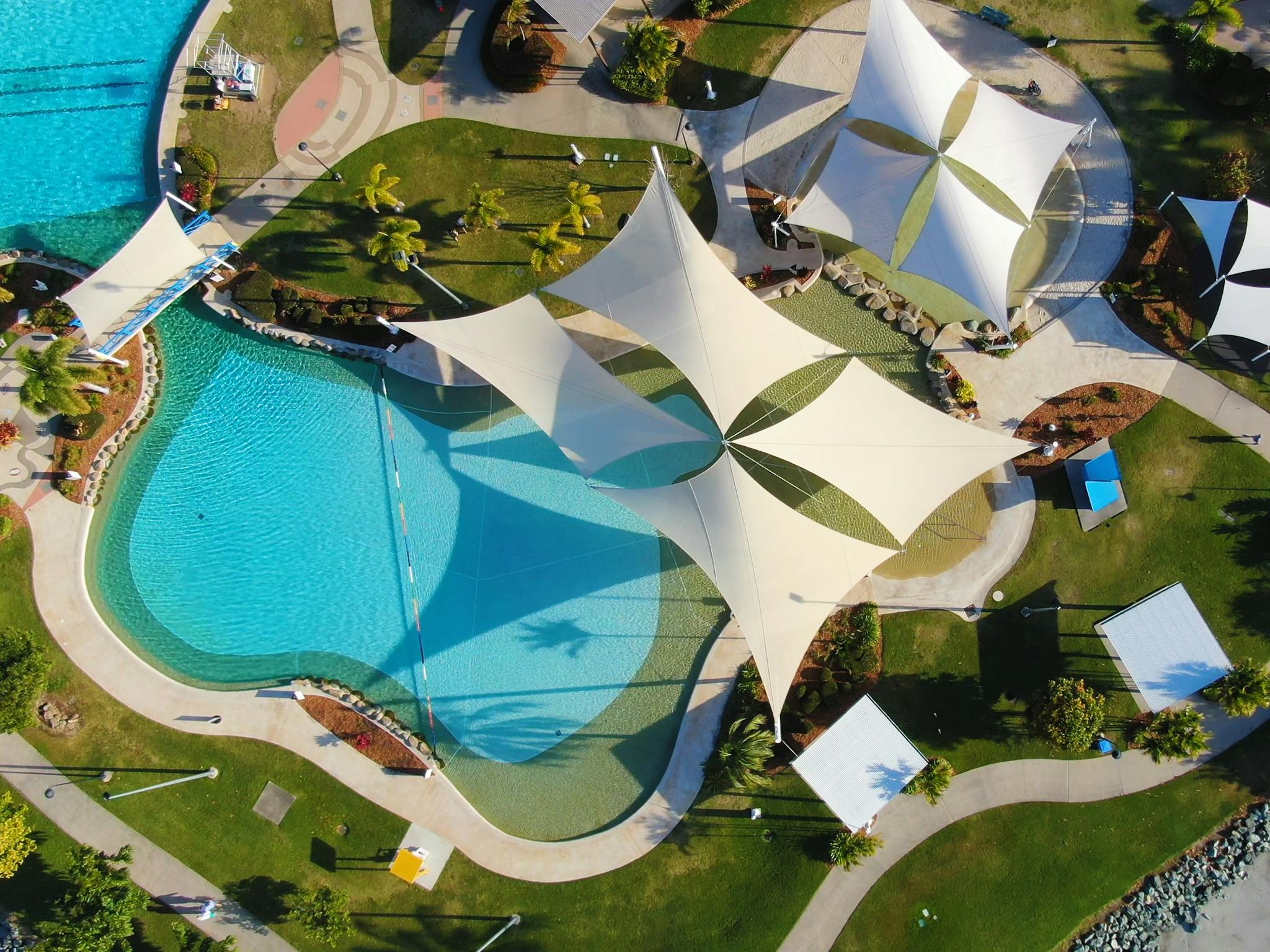 Aerial photo of Airlie Beach Lagoon showing swimming pool with bridge path,  gardens and shade saili