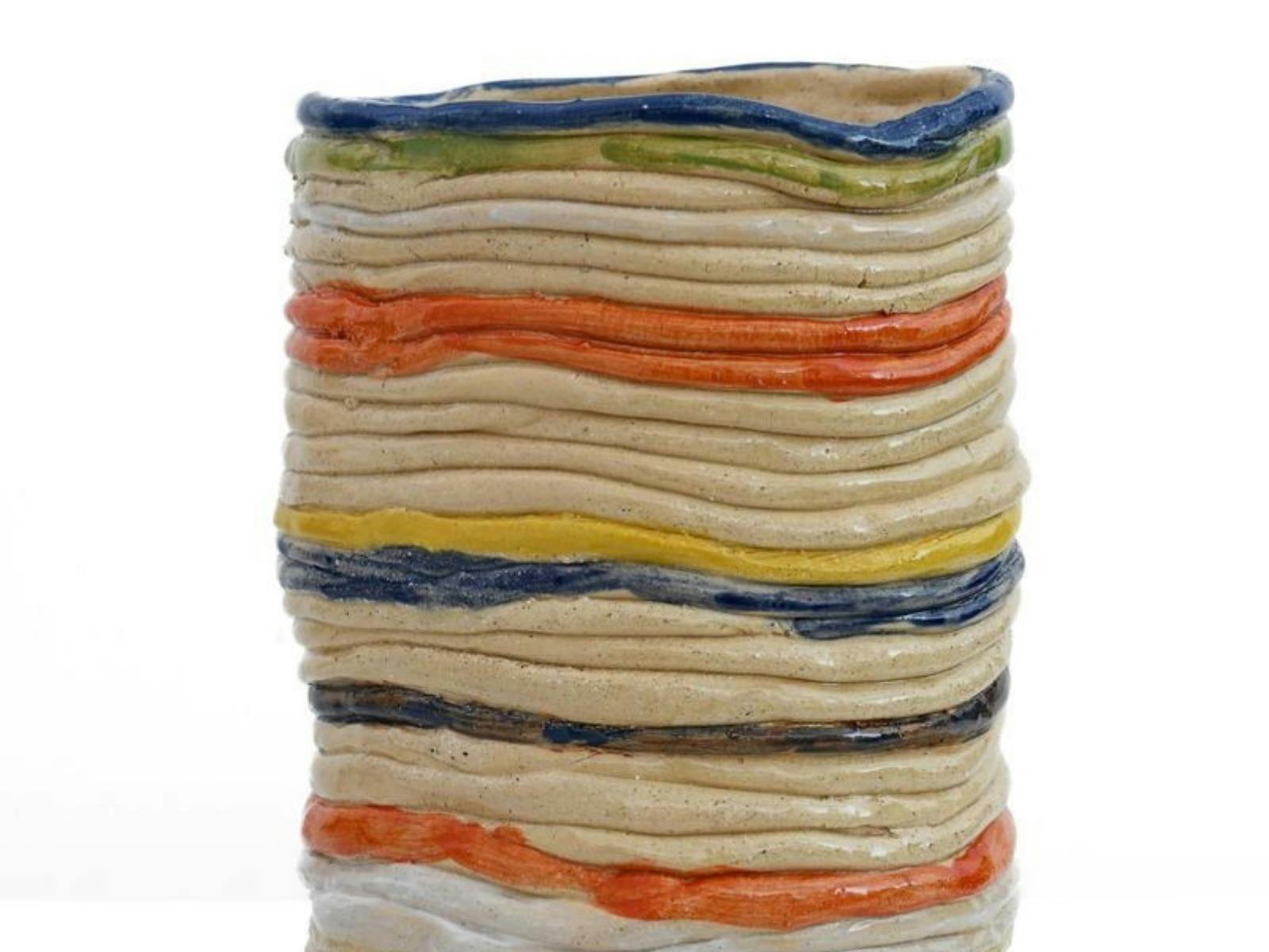 A hand-built ceramic vase with layered, uneven rings in earthy tones, featuring blue, yellow, orang