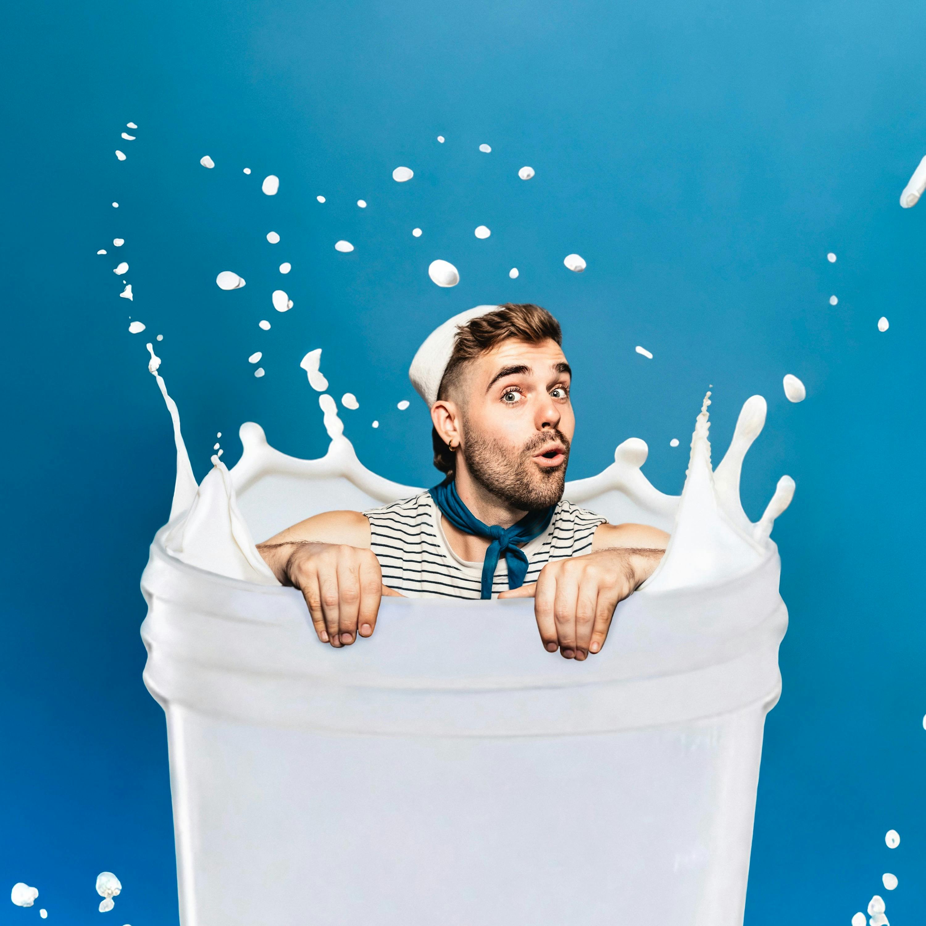A man in a striped shirt appears to be sitting in a container of milk, with milk splashing around