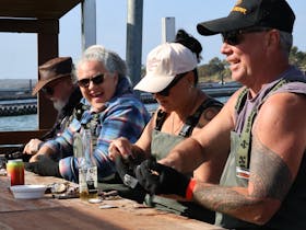 Guests shucking oysters and enjoying drinks at a Coffin Bay oyster farm tour, South Australia