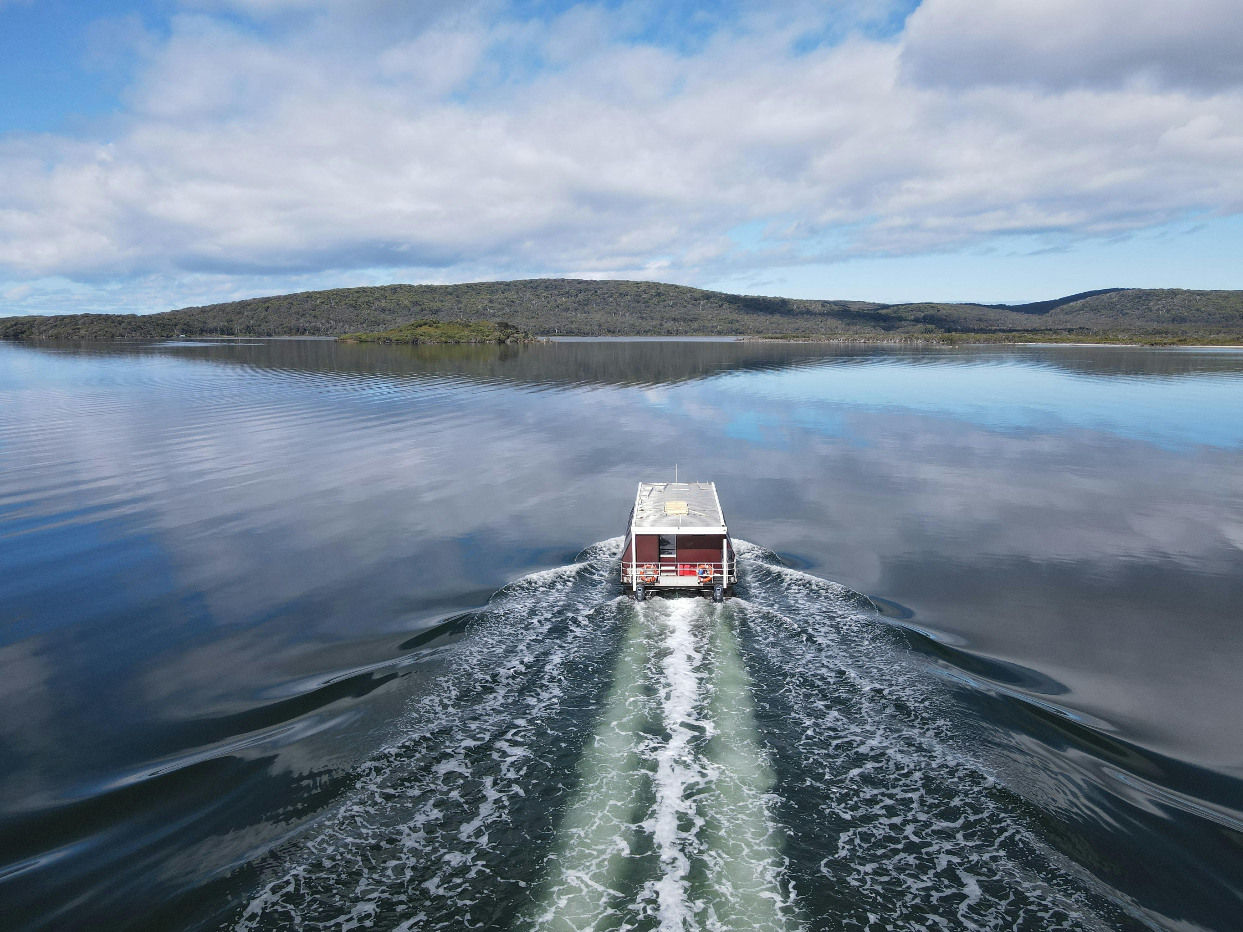 Drone photograph of small cruise boat in tranquil water driving towards island covered in trees