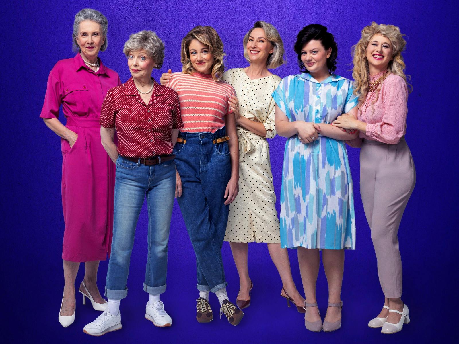 Six women stand side by side in colorful 1980s-style outfits against a purple background