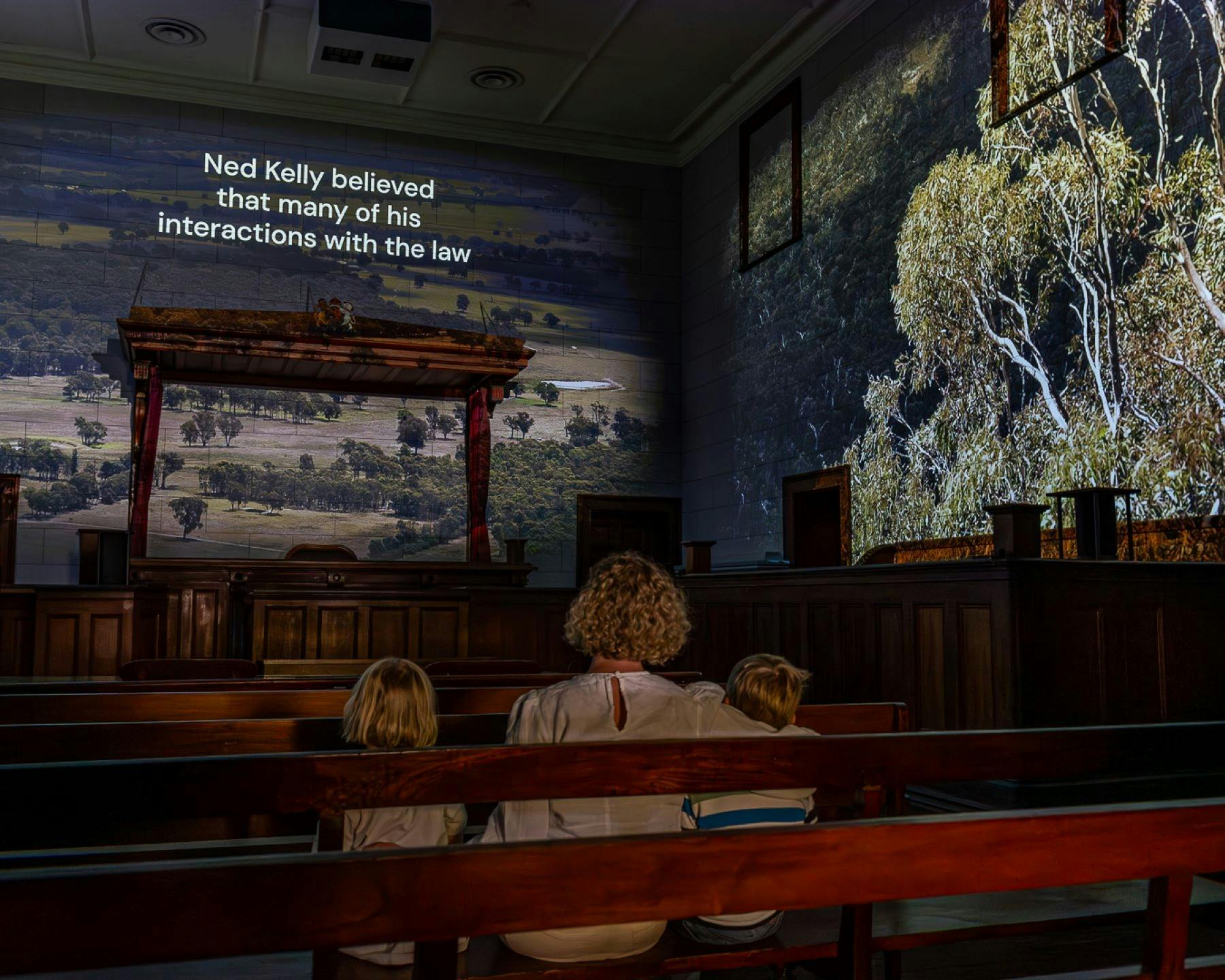 A family viewing the exhibition, the room lit softly and images of the countryside projected on wall