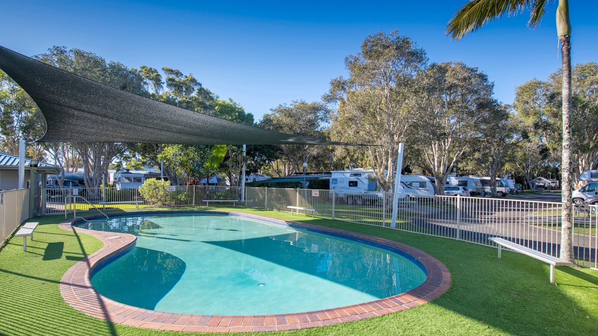 Shot of Mudjimba Beach Holiday Park swimming pool with no one swimming. Surrounded by trees and sun