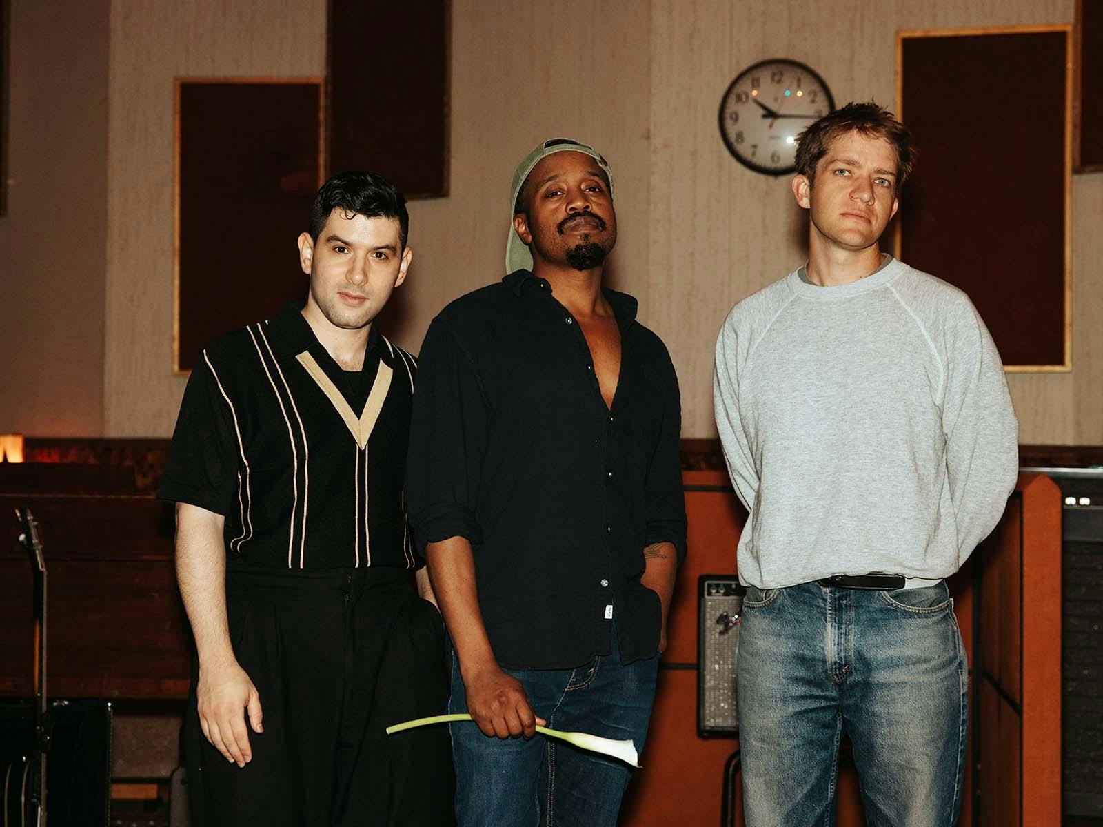 Three members standing in a laidback style looing at the camera.